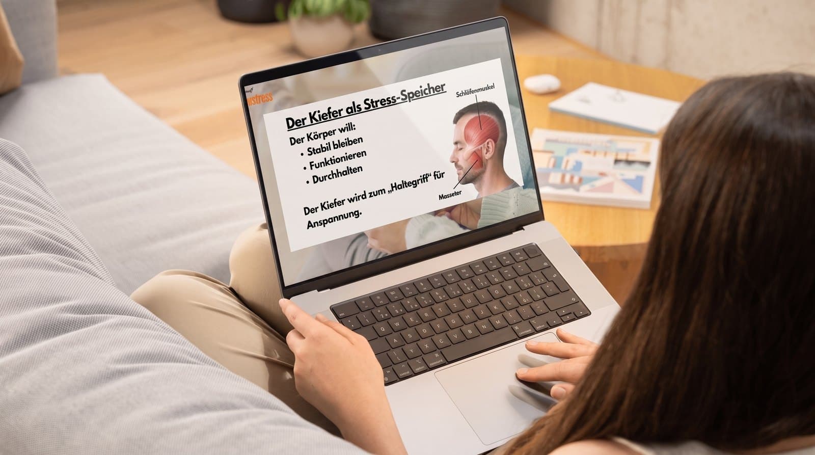Frau sitzt mit dem Laptop auf dem Sofa und schaut eine Kurseinheit des Programms an
