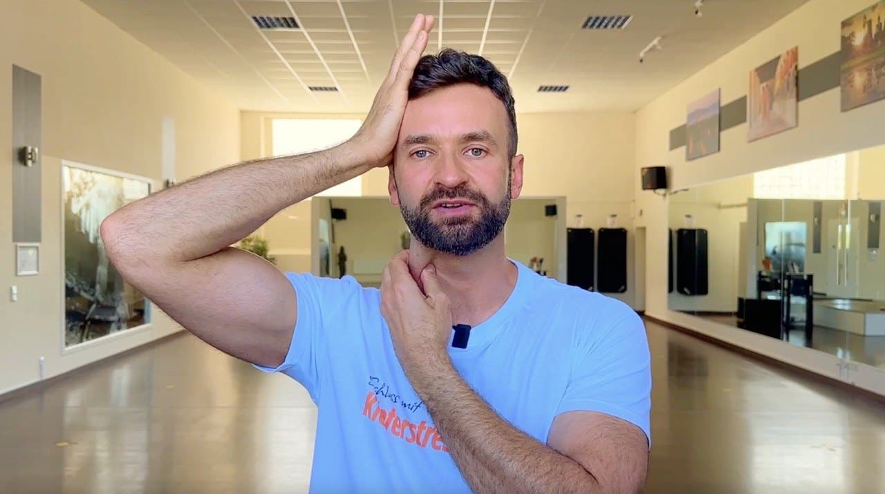 Robert Lazik führt eine Übung vor: eine Hand liegt seitlich am Kopf, die andere am Hals