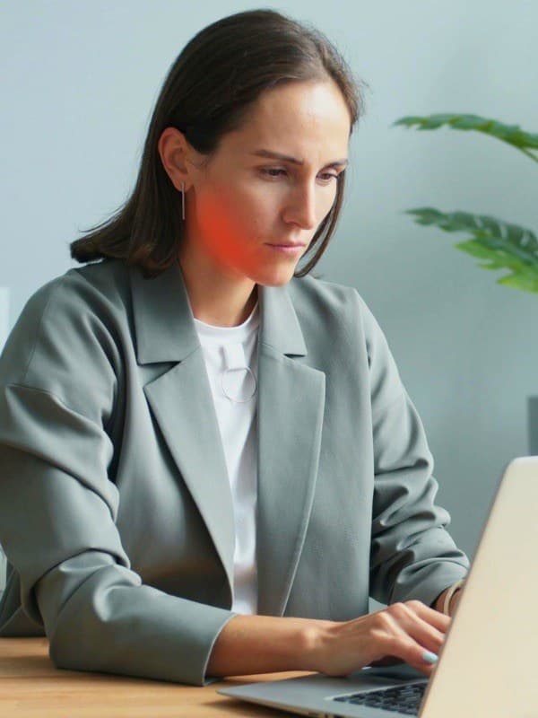 Frau arbeitet konzentriert am Laptop, der Kieferbereich ist als Spannungszone hervorgehoben